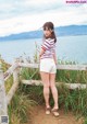 A woman standing next to a wooden fence by the water.