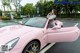 A woman sitting in the driver's seat of a pink sports car.