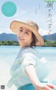 A woman in a straw hat sitting on a beach.